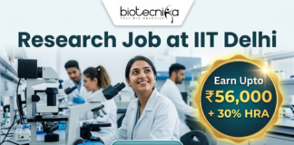 Research Job in Biomedical Engineering at IIT Delhi | Earn ₹56,000 per month Research Job in Biomedical Engineering at IIT Delhi | Earn ₹56,000 per month. Corporate-style job featured image banner (1280x720) for "Research Job at IIT Delhi" featuring the Biotecnika logo at the top center. The background shows a realistic, modern laboratory where a smiling young Indian female researcher in a white lab coat sits with a microscope, while two colleagues work behind her. On the right, a prominent gold and teal circular badge highlights text reading "Earn Upto ₹56,000 + 30% HRA". A sleek teal "APPLY NOW" button is positioned at the bottom center.