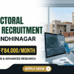 IIT Gandhinagar Postdoctoral Fellowship | Earn Up to ₹84,000/Month in Biomedical Research IIT Gandhinagar Postdoctoral Fellowship Earn Up to ₹84,000Month in Biomedical Research A corporate-style promotional banner for "Postdoctoral Fellow Recruitment at IIT Gandhinagar". The top left displays the Biotecnika logo, followed by bold text that reads "POSTDOCTORAL FELLOW RECRUITMENT at IIT GANDHINAGAR". A highlighted black and gold badge reads "EARN UPTO ₹84,000/MONTH", accompanied by the subtitle "GLOBAL EXPOSURE & ADVANCED RESEARCH". On the right side, a female researcher in a white lab coat, safety glasses, and blue gloves works at a computer monitor in a modern laboratory. Through the large window behind her, the iconic brick architecture of the IIT Gandhinagar campus is visible. A gold "APPLY NOW" button is positioned at the bottom center.