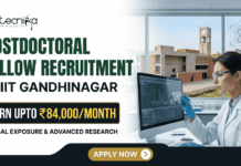 IIT Gandhinagar Postdoctoral Fellowship | Earn Up to ₹84,000/Month in Biomedical Research IIT Gandhinagar Postdoctoral Fellowship Earn Up to ₹84,000Month in Biomedical Research A corporate-style promotional banner for "Postdoctoral Fellow Recruitment at IIT Gandhinagar". The top left displays the Biotecnika logo, followed by bold text that reads "POSTDOCTORAL FELLOW RECRUITMENT at IIT GANDHINAGAR". A highlighted black and gold badge reads "EARN UPTO ₹84,000/MONTH", accompanied by the subtitle "GLOBAL EXPOSURE & ADVANCED RESEARCH". On the right side, a female researcher in a white lab coat, safety glasses, and blue gloves works at a computer monitor in a modern laboratory. Through the large window behind her, the iconic brick architecture of the IIT Gandhinagar campus is visible. A gold "APPLY NOW" button is positioned at the bottom center.