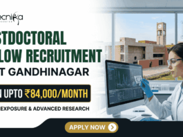 IIT Gandhinagar Postdoctoral Fellowship | Earn Up to ₹84,000/Month in Biomedical Research IIT Gandhinagar Postdoctoral Fellowship Earn Up to ₹84,000Month in Biomedical Research A corporate-style promotional banner for "Postdoctoral Fellow Recruitment at IIT Gandhinagar". The top left displays the Biotecnika logo, followed by bold text that reads "POSTDOCTORAL FELLOW RECRUITMENT at IIT GANDHINAGAR". A highlighted black and gold badge reads "EARN UPTO ₹84,000/MONTH", accompanied by the subtitle "GLOBAL EXPOSURE & ADVANCED RESEARCH". On the right side, a female researcher in a white lab coat, safety glasses, and blue gloves works at a computer monitor in a modern laboratory. Through the large window behind her, the iconic brick architecture of the IIT Gandhinagar campus is visible. A gold "APPLY NOW" button is positioned at the bottom center.