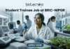 Student Trainee Job for Biotechnology & Life Science Students at BRIC-NIPGR Student Trainee Job for Biotechnology & Life Science Students at BRIC-NIPGR. A corporate-style job featured image banner (1280x720) for "Student Trainee Job at BRIC-NIPGR" featuring the Biotecnika CRO logo at the top center. The background showcases a realistic, high-tech plant biology research laboratory. A smiling young Indian female student trainee wearing a white lab coat, safety goggles, and blue gloves is using a pipette over a well plate. Trays of green plant seedlings are arranged on the lab counter alongside modern equipment, with other researchers working in the background. A clean, dark teal "APPLY NOW" button is centered at the bottom.